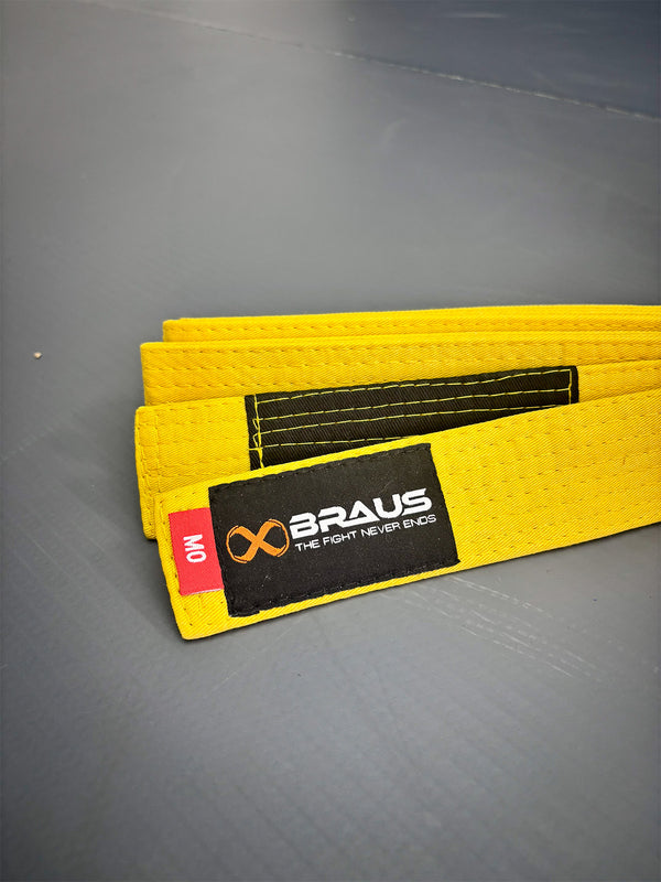 Yellow martial arts belt with Braus logo on a gray mat
