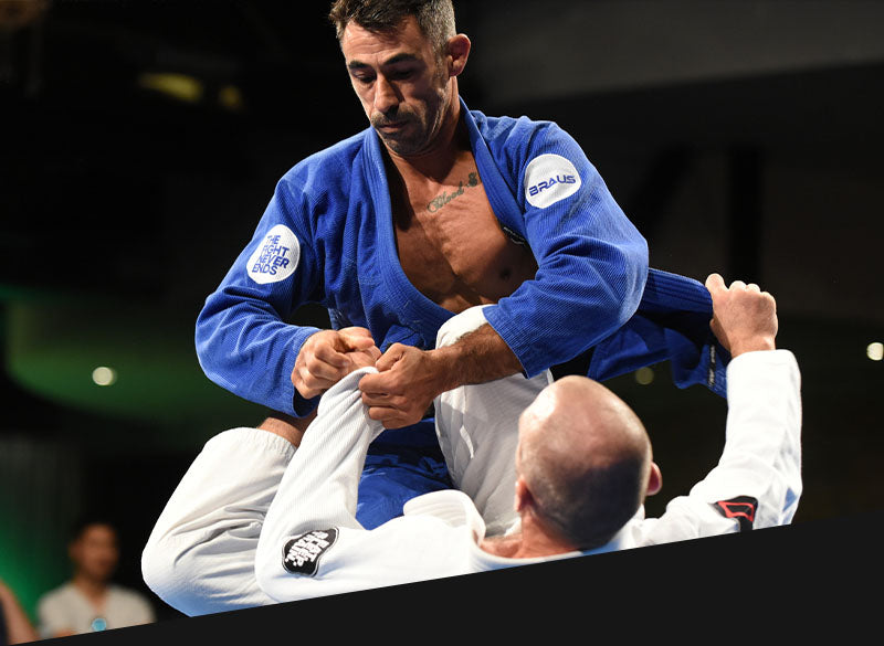 Brazilian Jiu Jitsu athletes in action during a BJJ match, showcasing a blue Braus Fight gi against a white gi, emphasizing technique and dynamic movement. Mobile Version