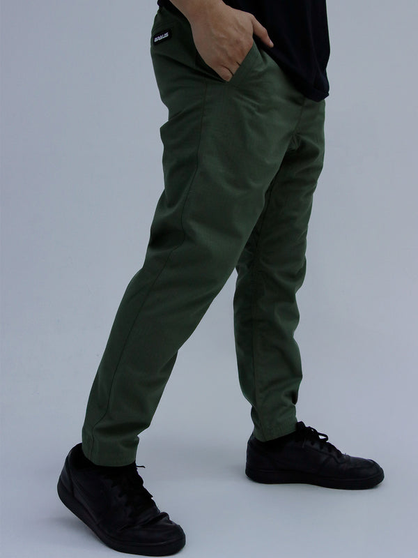 Person wearing army green pants and black shoes on a plain background