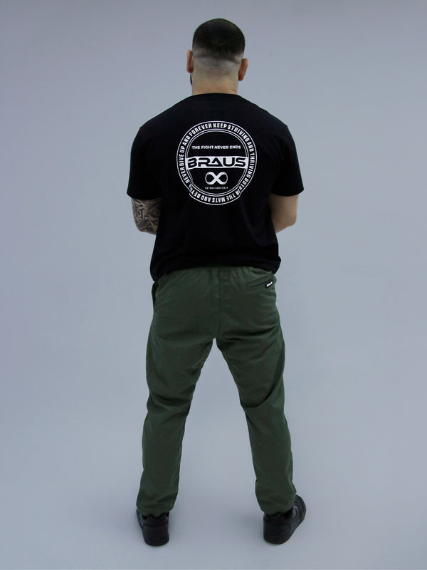 Person wearing a black t-shirt with a logo on the back, standing against a plain background army green pants.